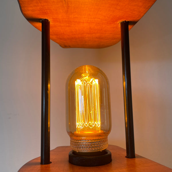 Reclaimed wood table lamp crafted with a split totara post and black metal rods, glow of  bulb, close up.