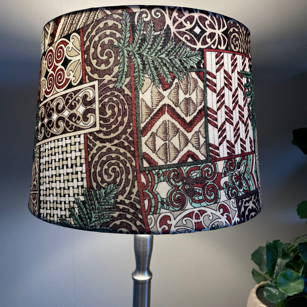 Shades at grays medium tapered handcrafted fabric lampshade, lit, close up.