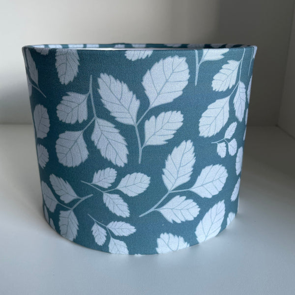 Small drum lampshade handcrafted by shades at grays with leaf slate blue fabric by Jade Ell, unlit.