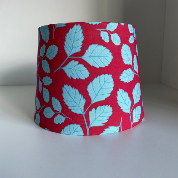 Small tapered lampshade handcrafted by shades at grays with leaf red fabric by Jade Ell, unlit.