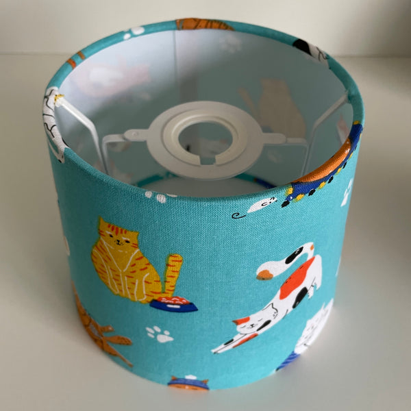 Small tapered lampshade with a flexible frame suitable for ceiling pendant or a table lamp, with a blue fabric shade featuring cat illustrations. 