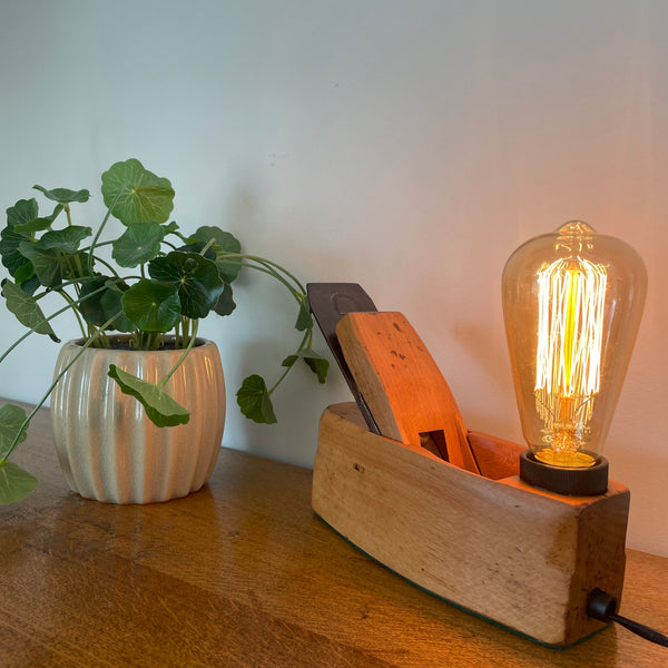 Small carpenters plane upcycled by shades at grays with added replica edison light bulb, lit, diagonal view.