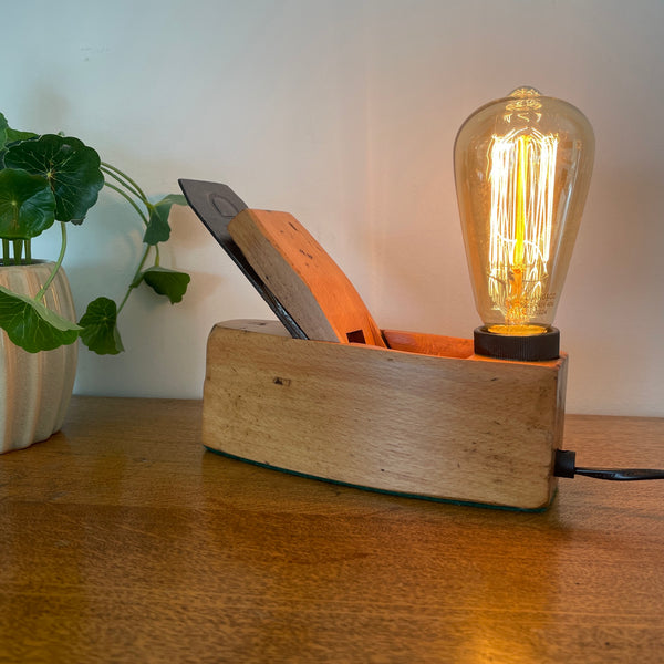 Small carpenters plane upcycled by shades at grays with added replica edison light bulb, lit,  front view.