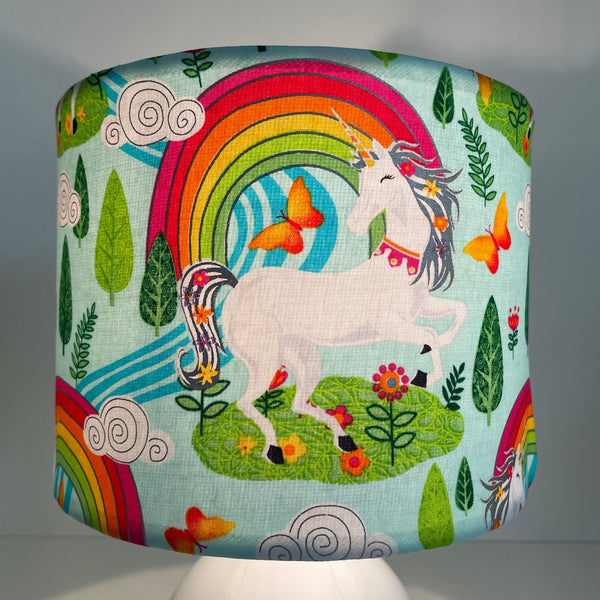 Small drum fabric lamp shade with white unicorn and orange butterflies, on white base, lit, close up.