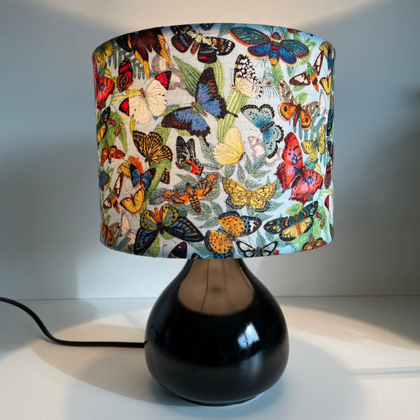 Small drum hand crafted fabric light shade, lit on black base.