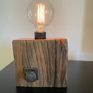 Smalll wood lamp crafted from recycled wharf timber with original bolt and edison bulb, lit by shades at grays.