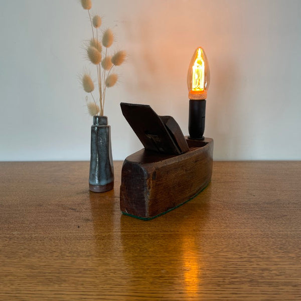 Small table lamp crafted by shades at grays from a vintage carpenter's plane, with a LED candle bulb, lit, back view.