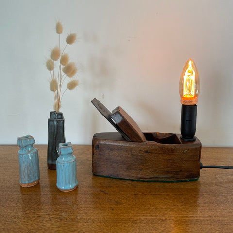 Small table lamp crafted by shades at grays from a vintage carpenter's plane, with a LED candle bulb, lit, front view.