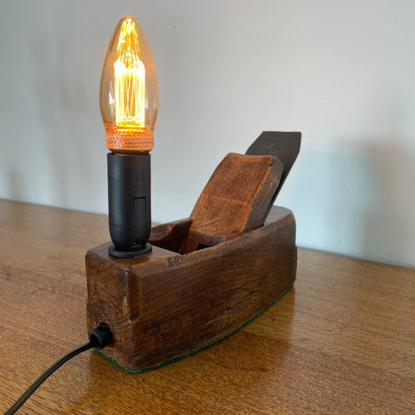 Small table lamp crafted by shades at grays from a vintage carpenter's plane, with a LED candle bulb, lit, side and back view.