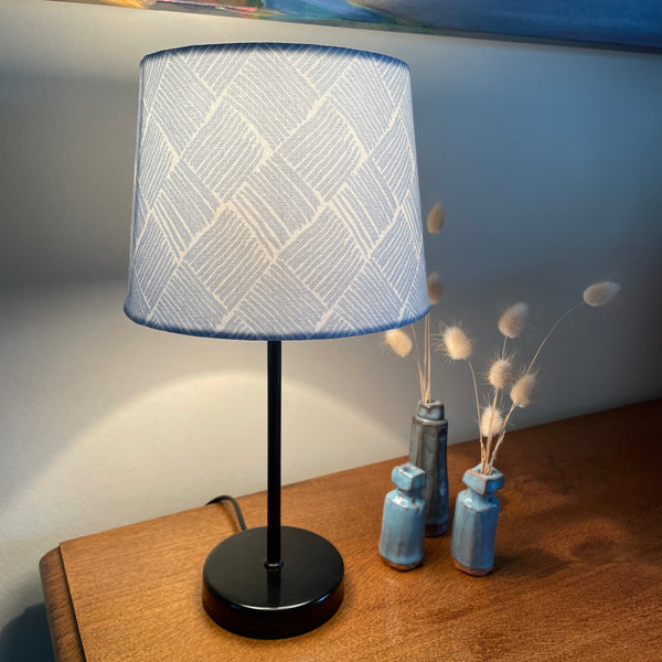 Small tapered handcrafted fabric lamp shade, lit on black base.
