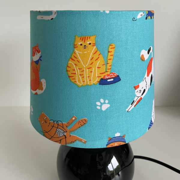 Lamp with a blue fabric shade featuring cat illustrations on a small black base, unlit.