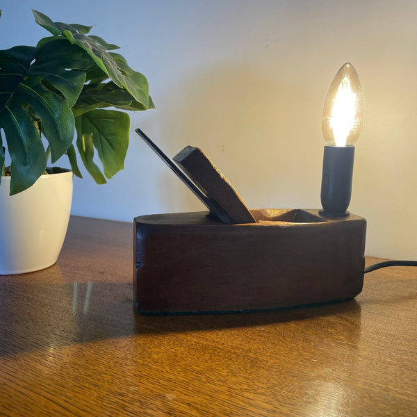 Desk lamp with a light bulb on a wooden surface next to a plant