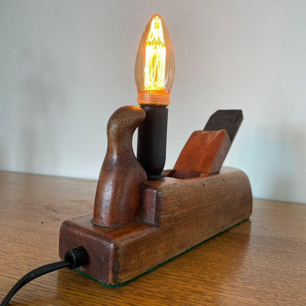 Table lamp handcrafted by shades at grays from authentic carpenter's plane, with LED candle E14 bulb, lit, back and side view.