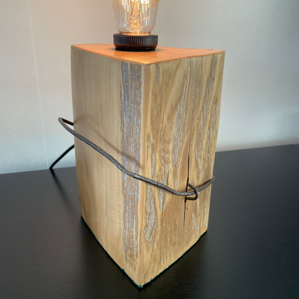 Table lamp crafted by shades at grays, nz, from old tōtara fence post with original iron, angled side view, lit.