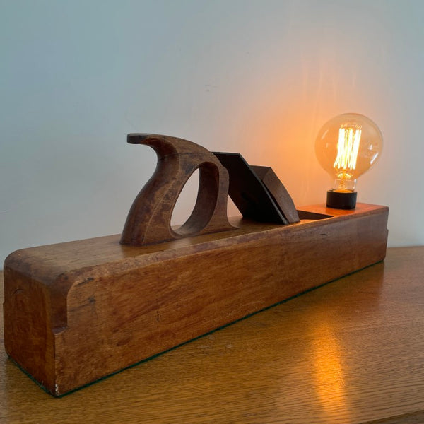 Table lamp crafted by shades at grays from large vintage carpenter's plane with edison bulb, lit, back and side view.