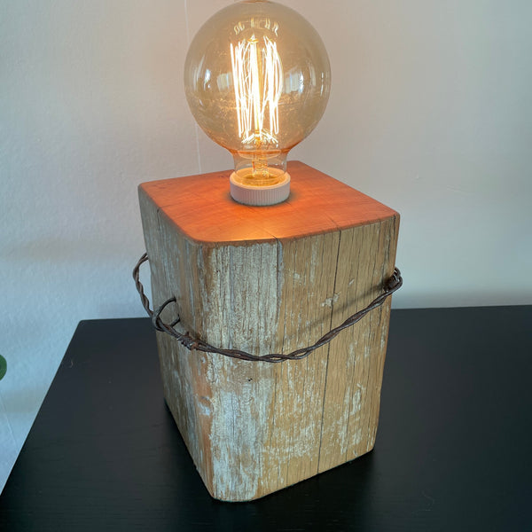 Table lamp crafted by shades at grays from old tōtara fence post with original barb wire, front and side view, lit.