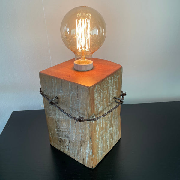 Table lamp crafted by shades at grays from old tōtara fence post with original barb wire, back and side view, lit.