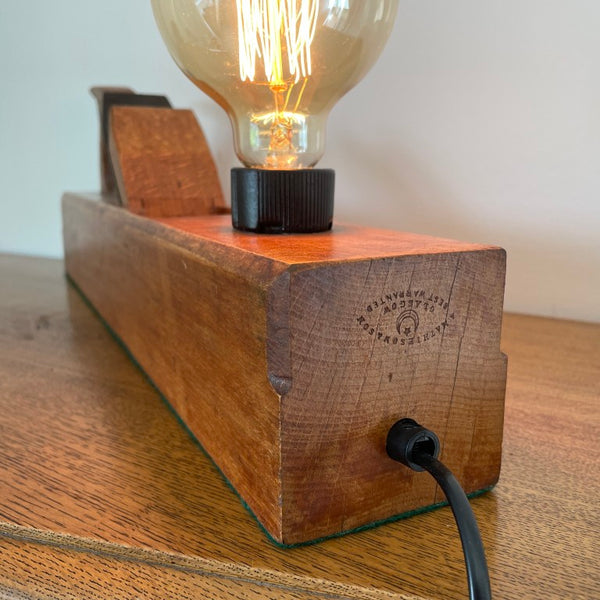 Table lamp crafted from large vintage carpenter's plane with edison bulb, lit, close up of manufacturer's stamp.