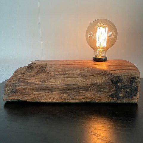 Table lamp crafted from reclaimed wharf timber, with replica edison bulb providing reflection on black table top.