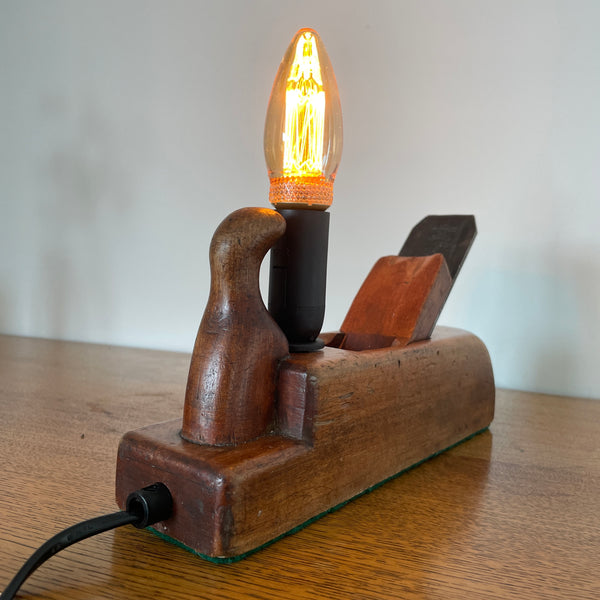 Table lamp handcrafted by shades at grays from authentic carpenter's plane, with LED candle E14 bulb, lit, back and side view.