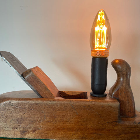 Table lamp handcrafted by shades at grays from authentic carpenter's plane, with LED candle E14 bulb, lit, close up.