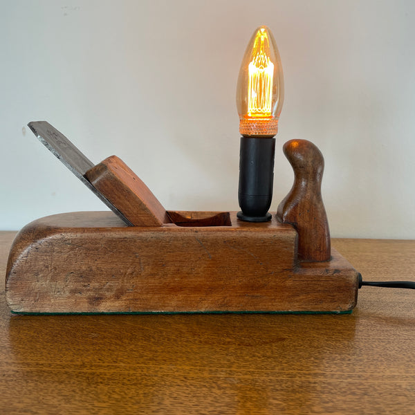 Table lamp handcrafted by shades at grays from authentic carpenter's plane, with LED candle E14 bulb, lit, front view.