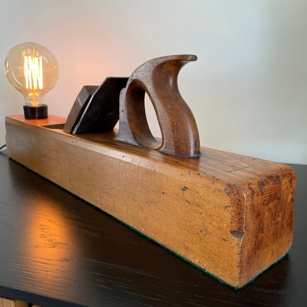 Table lamp made from authentic wood plane by shades at grays, nz, reflected light of edison bulb on cabinet.