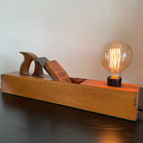 Table lamp made from authentic wood plane by shades at grays, nz, warm golden wood, angled view. Lit.