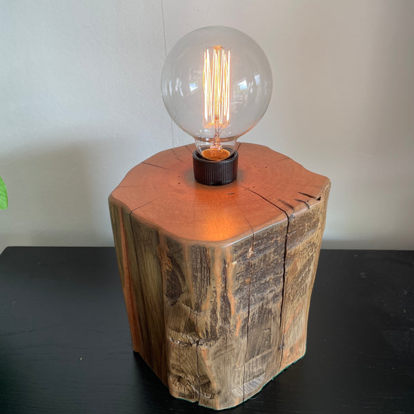 Tōtara fence post table lamp from Shades at Grays  long view of polished top and front view, with axe marks and edison bulb, lit.