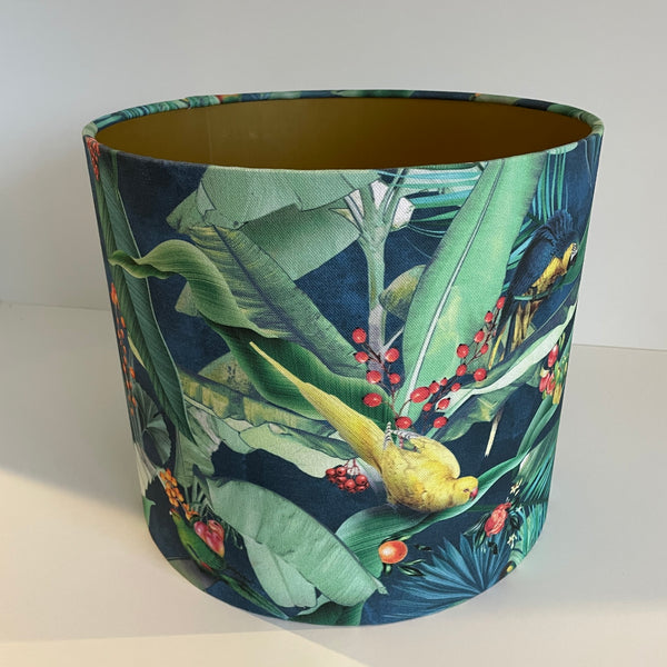 Tropical bird fabric medium drum lampshade, with gold inner, and yellow parrot, perched among red berries and green foliage.