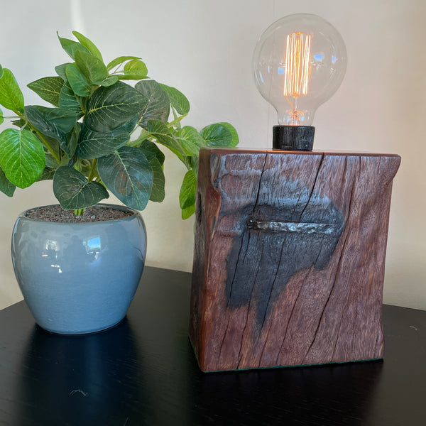 Deep red wood of table lamp handcrafted from 100 year old wharf timber by shades at grays, front viewlit.