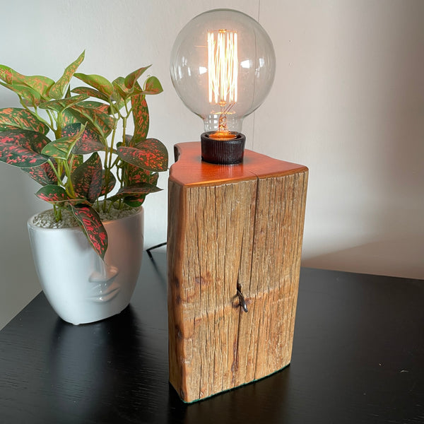 Wood table lamp handcrafted by shades at grays from reclaimed totara fence post, with old staple in postion, front view, lit by shades at grays.