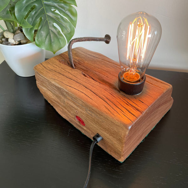 Rustic reclaimed wharf timber table lamp crafted by shades at grays, nz, with original iron nail, lit, back view with black lead.