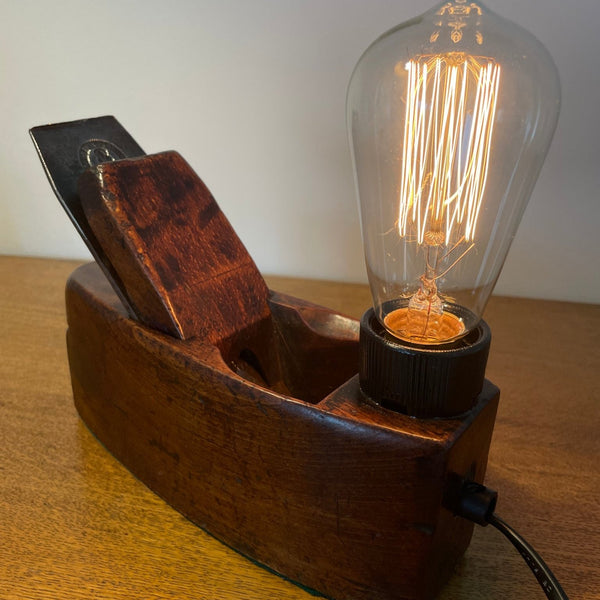 Wood table lamp crafted from authentic carpenters plane, dating back 100 plus years, with replica edison bulb, lit, sold by shades at grays.