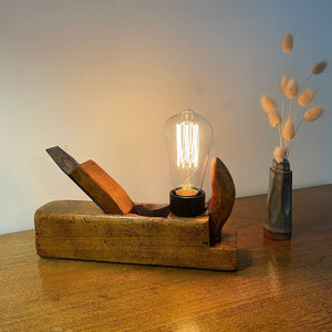 Wood table lamp crafted from authentic carpenters plane, with replica teardrop bulb, lit,front view by shades at grays