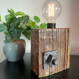 Unique wood lamp created from reclaimed wharf timber, with replica edison bulb, lit. Front view.