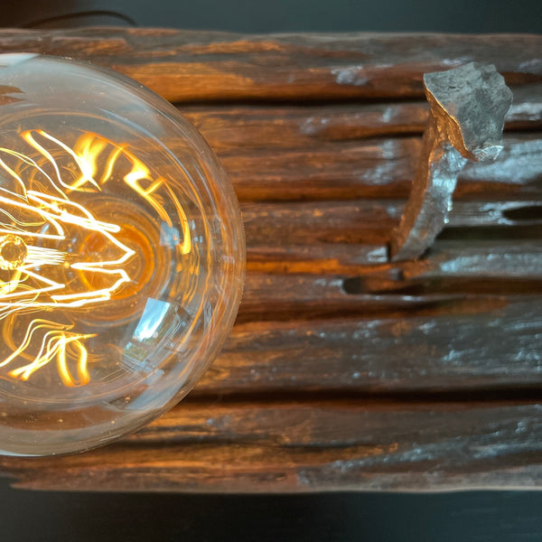 Hand crafted wood lamp created from old railway sleeper with replica edison bulb, lit, made by shades at grays, close up of retained original spike and bulb.