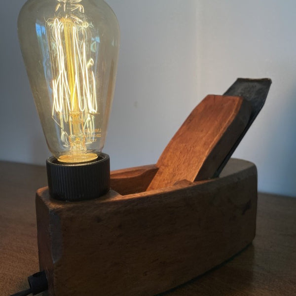 Upcycled carpenter's plane into wood table lamp by shades at grays with replica edison bulb, lit, close up.