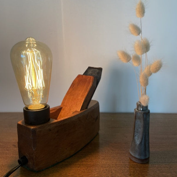 Upcycled carpenter's plane into wood table lamp by shades at grays with replica edison bulb, lit, long view.