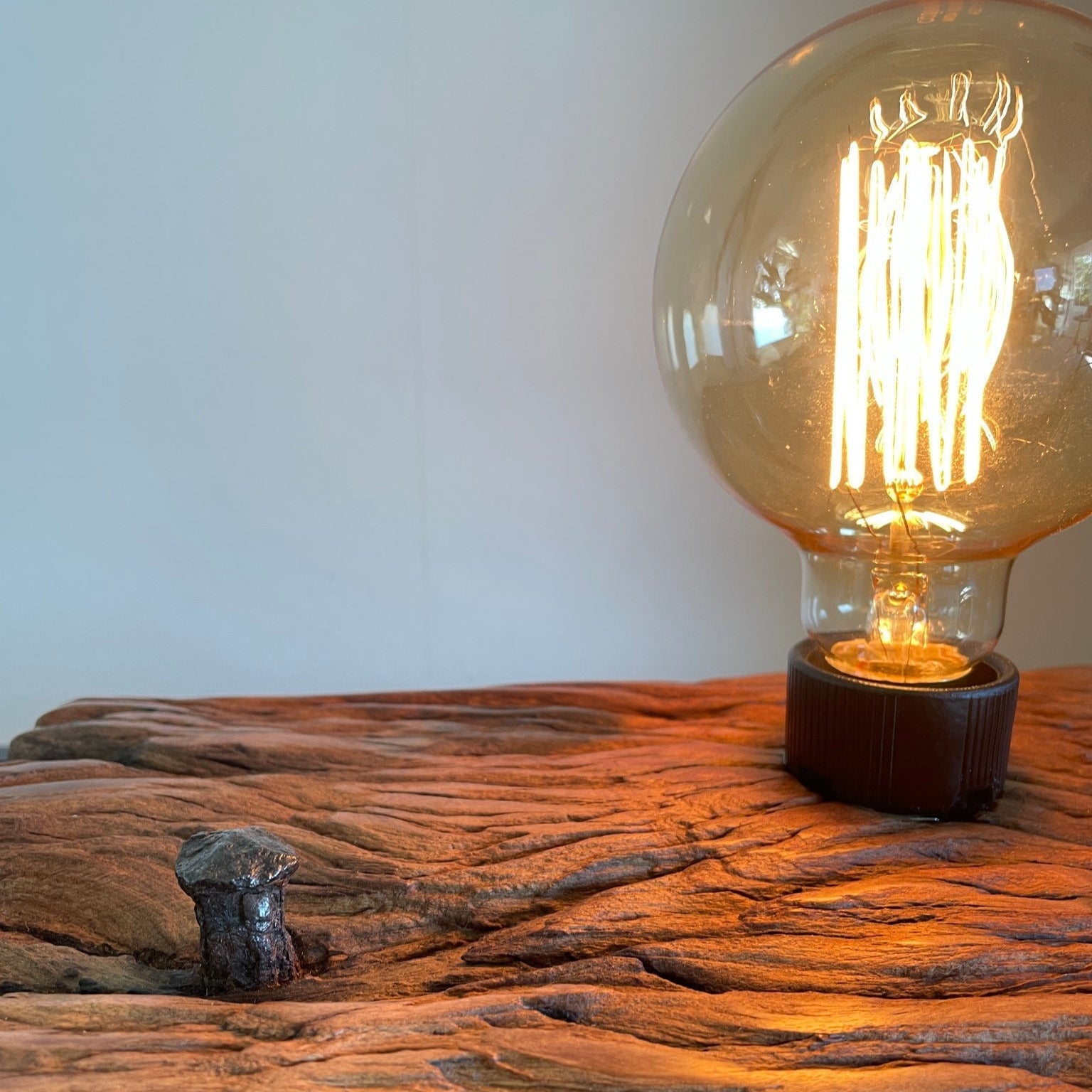 Upcycled wharf timber table lamp, handcrafted by shades at grays, close up view of erosion lines and original nail, with edison lamp, lit.