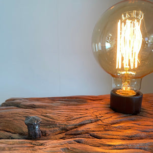 Upcycled wharf timber table lamp, handcrafted by shades at grays, close up view of erosion lines and original nail, with edison lamp, lit.