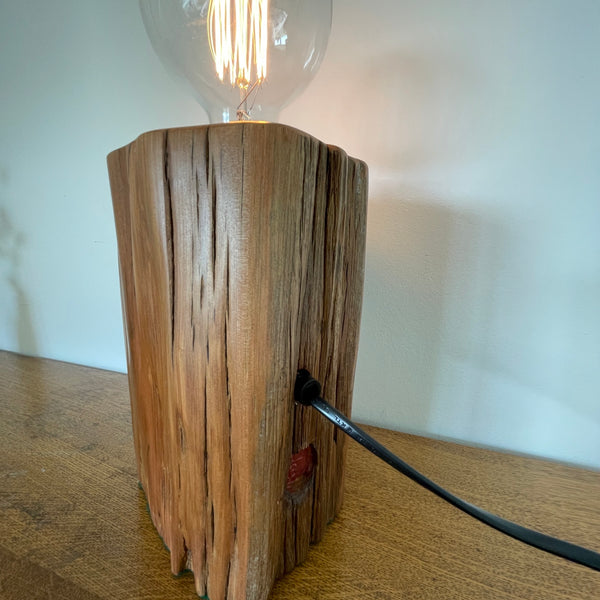 Upcycled wood lamp handcrafted by shades at grays from vintage totara post side and back view with black lead, lit.