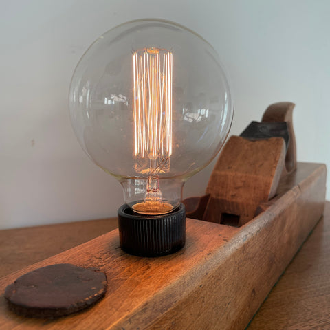 Upcycled wood plane table lamp handcrafted from vintage carpenters plane and additional edison bulb, lit, by shades at grays.