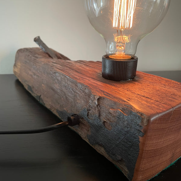 Upcycled wood table lamp from origianl wharf timber, vintage nail and replica edison bulb, lit, back view with black lead, handcrafted by shades at grays.