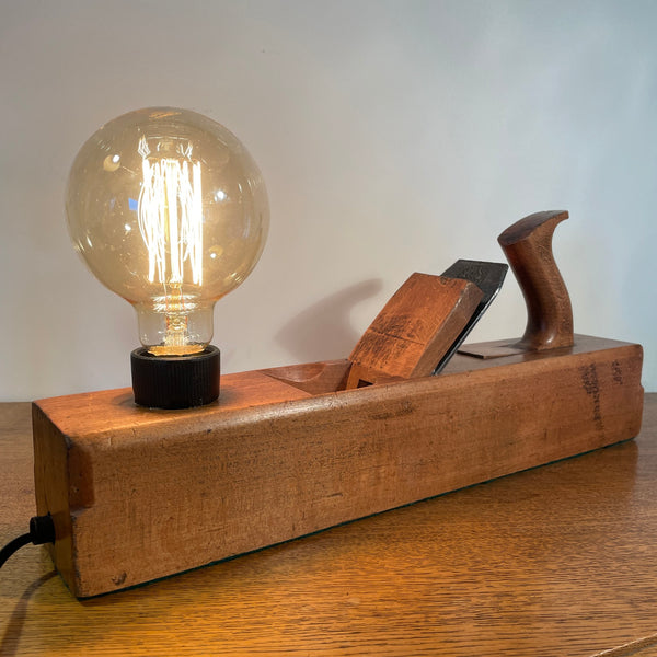 Vintage carpenters plane with replica edison bulb, lit, front and side view with black lead, crafted by shades at grays.