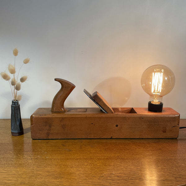 Vintage carpenters plane with replica edison bulb, lit, front view by shades at grays.