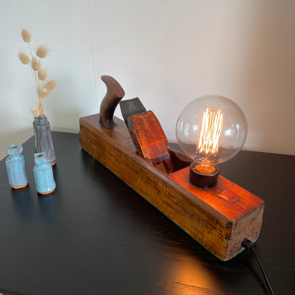 Vintage carpenter's wood plane table lamp crafted by shades at grays, angled view, lit.