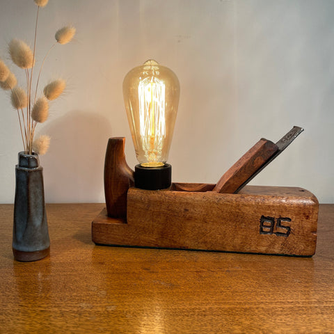 Vintage carpenters plane with replica edison lamp and authentic carpenter's initials, front view, lit.