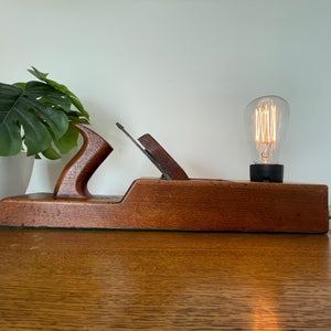 Vintage carpentry wood plane table lamp from Shades at Grays, long front view with edison bulb, lit.