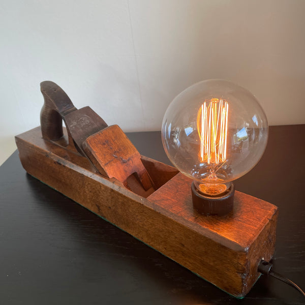 Vintage lamp crafted by shades at grays from an antique carpenters' plane, with edison bulb, lit.